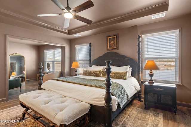 bedroom featuring visible vents, ornamental molding, a raised ceiling, and wood finished floors