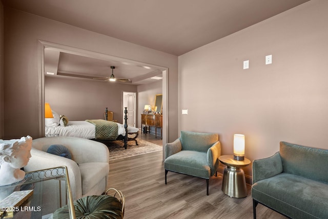 bedroom with ceiling fan, a tray ceiling, and wood finished floors