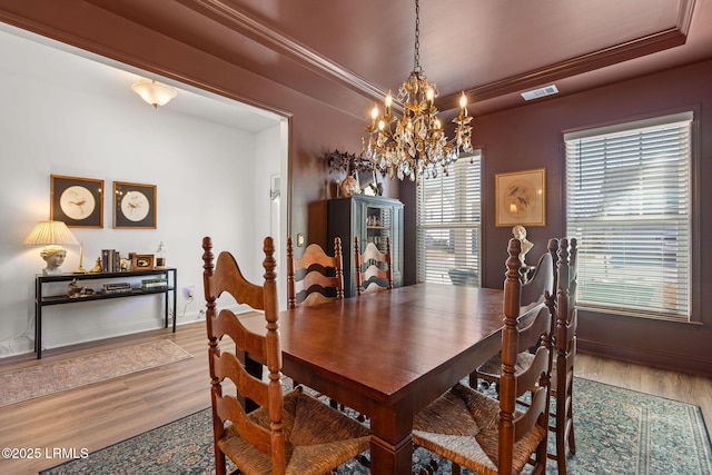 dining area featuring a raised ceiling, crown molding, hardwood / wood-style flooring, and an inviting chandelier