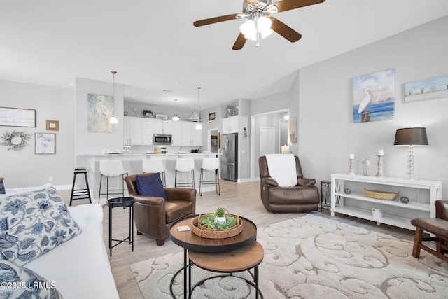 living area with baseboards, light wood-type flooring, and ceiling fan