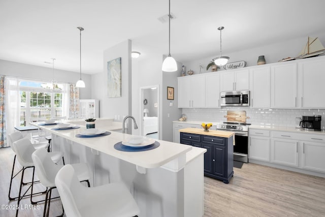 kitchen with tasteful backsplash, light wood-type flooring, white cabinets, stainless steel appliances, and a kitchen island with sink