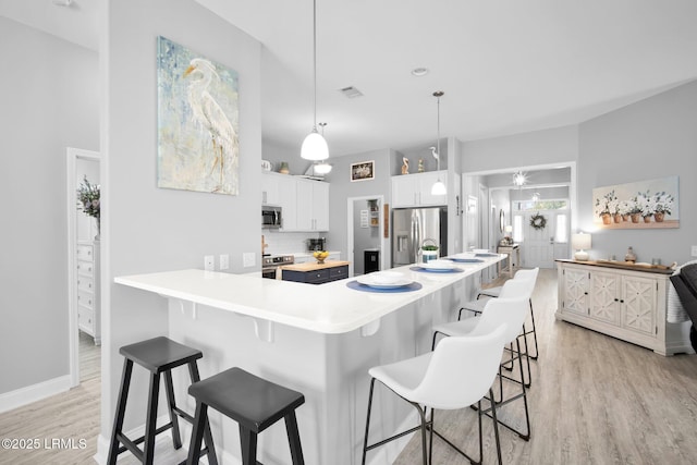 kitchen featuring a kitchen bar, white cabinetry, hanging light fixtures, light hardwood / wood-style flooring, and appliances with stainless steel finishes