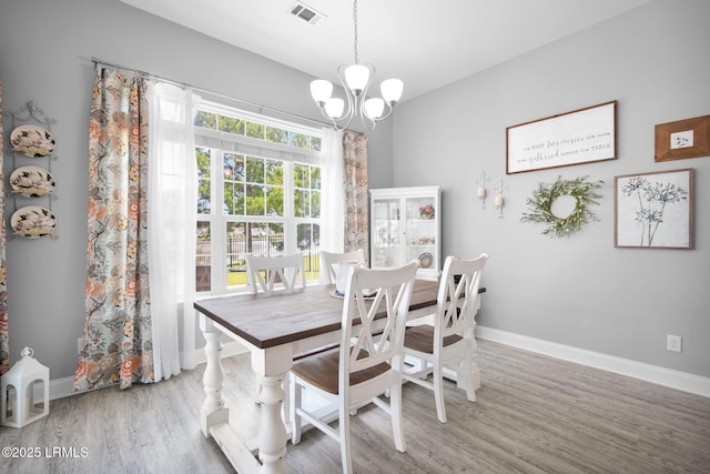 dining area with baseboards, wood finished floors, visible vents, and a chandelier