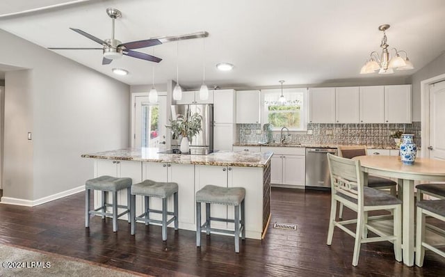 kitchen featuring appliances with stainless steel finishes, white cabinets, a kitchen island, decorative light fixtures, and vaulted ceiling