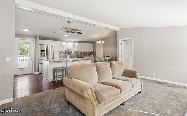 carpeted living room featuring vaulted ceiling with beams and ceiling fan with notable chandelier