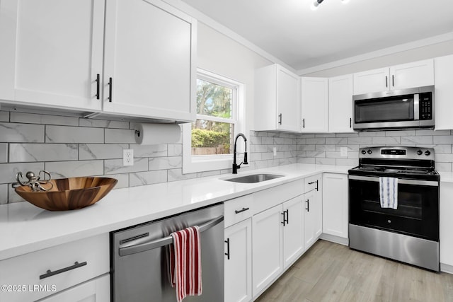kitchen with tasteful backsplash, white cabinets, a sink, stainless steel appliances, and light countertops