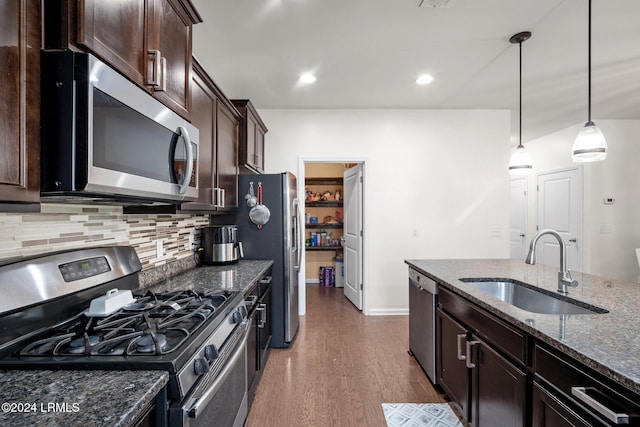 kitchen with sink, hanging light fixtures, appliances with stainless steel finishes, dark stone counters, and decorative backsplash