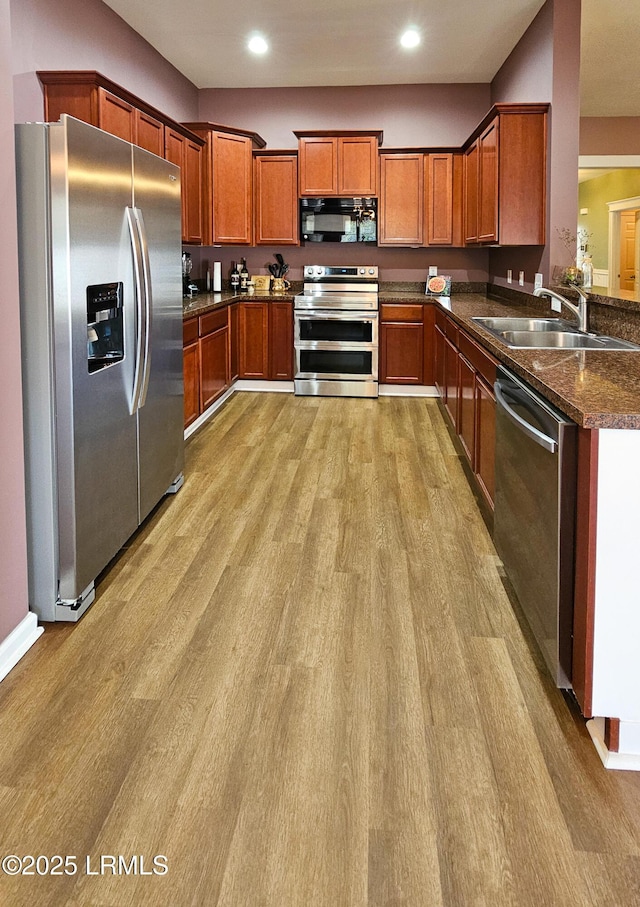 kitchen featuring brown cabinets, light wood finished floors, recessed lighting, appliances with stainless steel finishes, and a sink