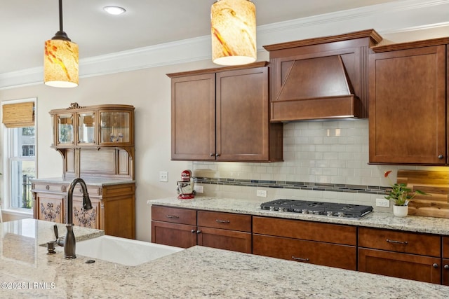 kitchen featuring backsplash, crown molding, stainless steel gas cooktop, custom exhaust hood, and a sink