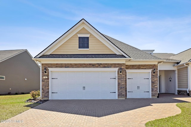 view of front facade with a shingled roof, decorative driveway, and a garage