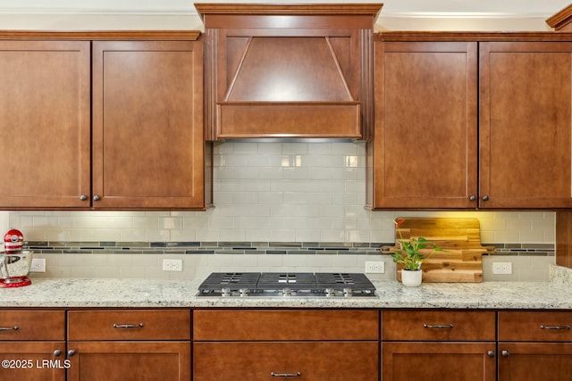 kitchen featuring stainless steel gas stovetop, wall chimney exhaust hood, tasteful backsplash, and light stone counters