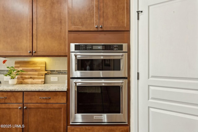 kitchen featuring decorative backsplash, light stone countertops, double oven, and brown cabinets