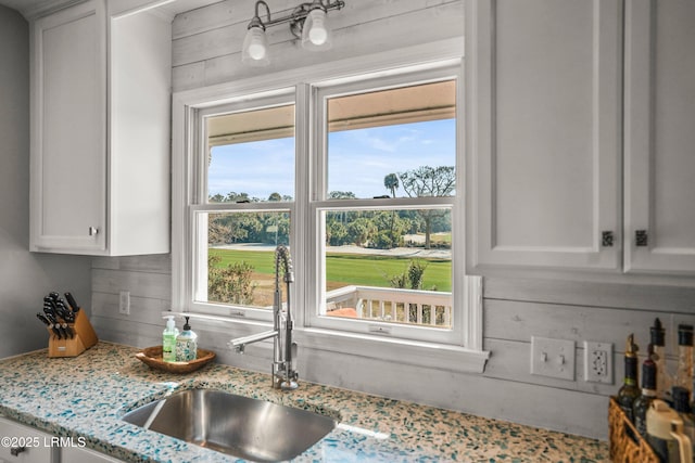 kitchen with white cabinets, a sink, wooden walls, and light stone countertops