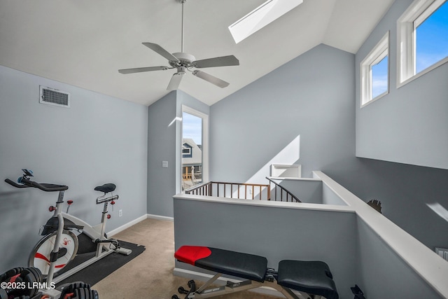 workout area with carpet, visible vents, ceiling fan, vaulted ceiling with skylight, and baseboards