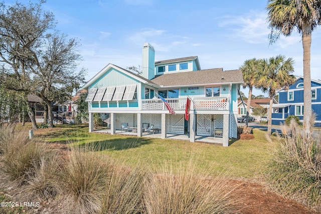 back of property featuring a deck, a patio area, a lawn, and a chimney