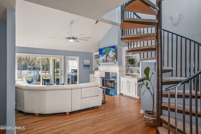 living room with a tile fireplace, ceiling fan, wood finished floors, stairs, and high vaulted ceiling