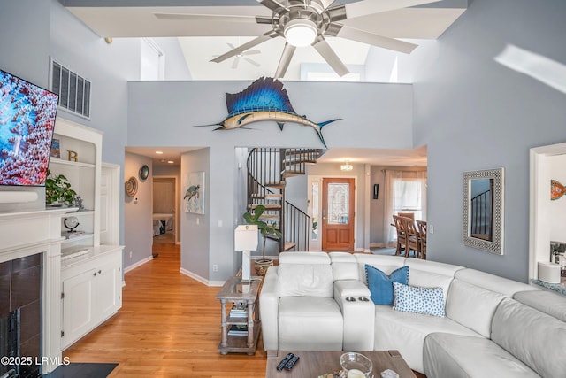 living room featuring light wood finished floors, visible vents, a ceiling fan, stairway, and a fireplace