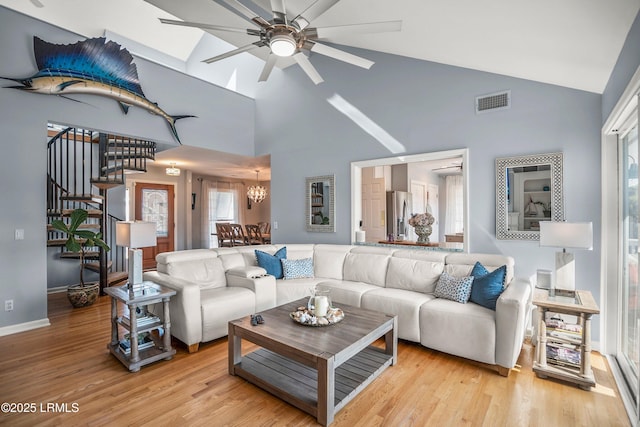 living area featuring light wood finished floors, stairs, visible vents, and high vaulted ceiling