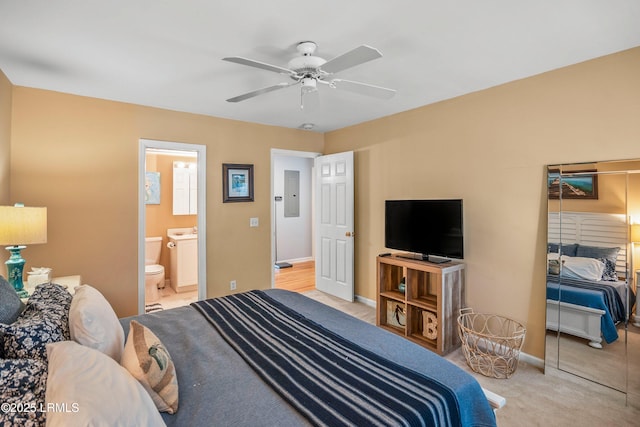 bedroom featuring ceiling fan, light colored carpet, baseboards, electric panel, and ensuite bath