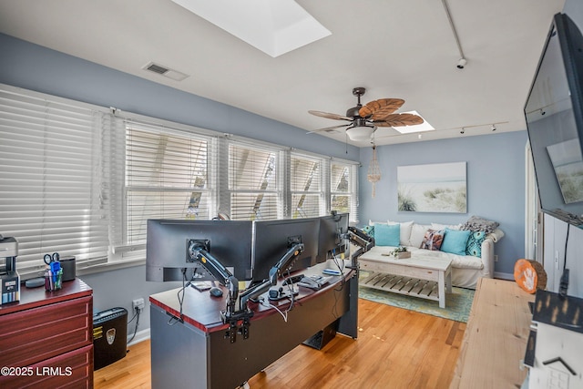 home office with a skylight, a ceiling fan, wood finished floors, and rail lighting