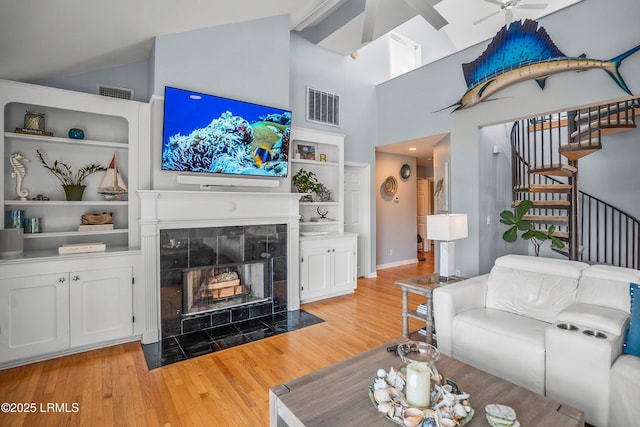 living room with a tile fireplace, visible vents, built in features, stairs, and light wood finished floors