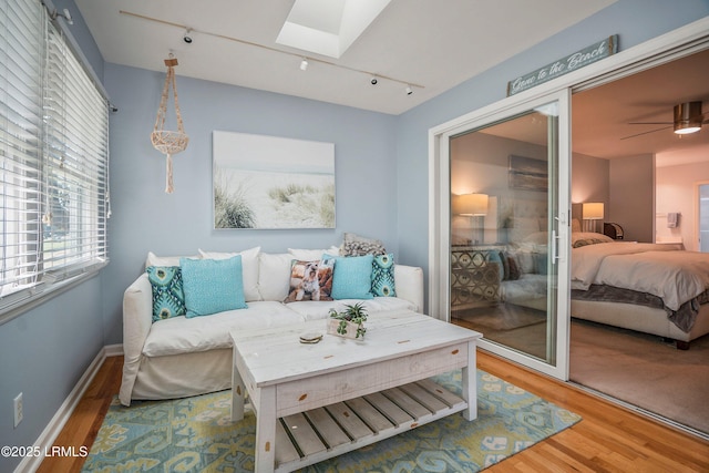 living room with a skylight, baseboards, a ceiling fan, wood finished floors, and track lighting