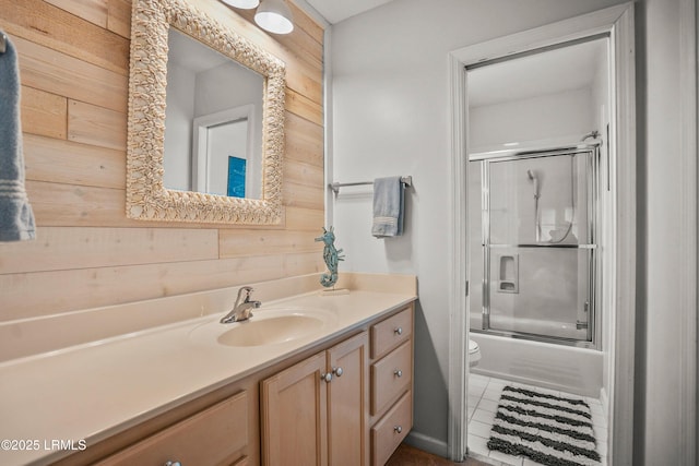 full bath featuring wooden walls, shower / bath combination with glass door, vanity, and toilet