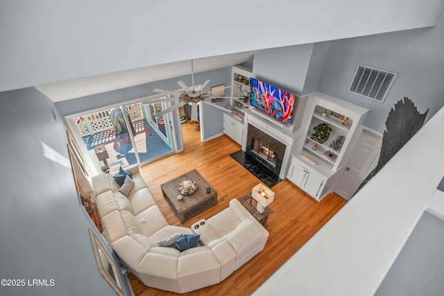 living room with a fireplace with flush hearth, visible vents, vaulted ceiling, and light wood-style flooring