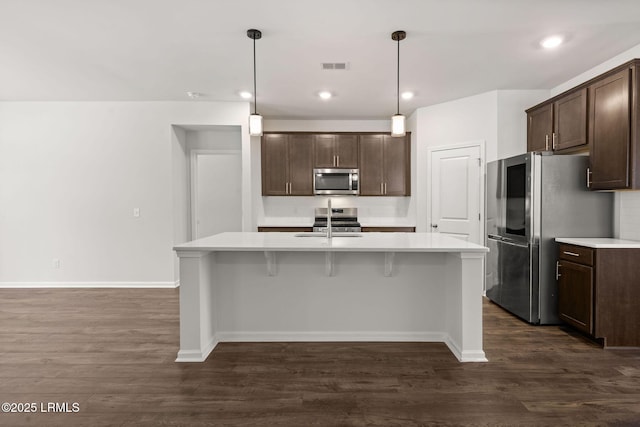 kitchen with light countertops, dark brown cabinets, appliances with stainless steel finishes, and a center island with sink