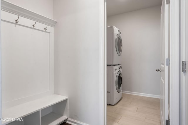 laundry room featuring laundry area, stacked washer and dryer, light wood-style flooring, and baseboards