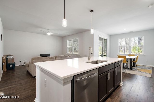 kitchen with a sink, stainless steel dishwasher, dark wood finished floors, light countertops, and hanging light fixtures