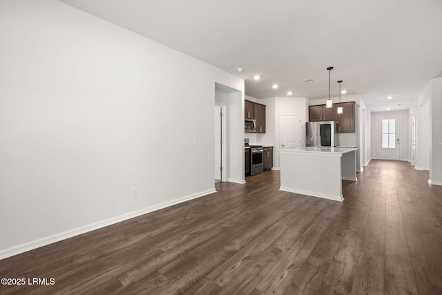 interior space featuring appliances with stainless steel finishes, a center island with sink, recessed lighting, open floor plan, and dark wood-style floors