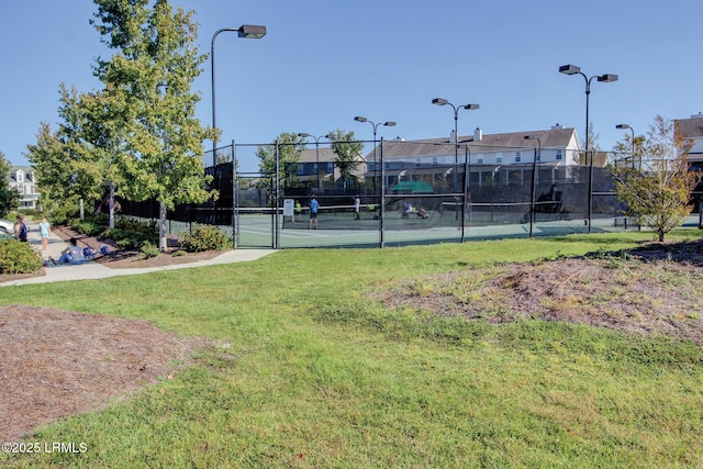 view of tennis court with a residential view, a lawn, and fence