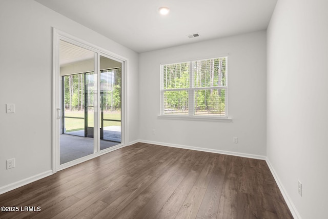 unfurnished room with dark wood-style flooring, baseboards, visible vents, and a wealth of natural light