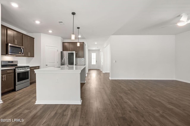 kitchen featuring dark brown cabinetry, appliances with stainless steel finishes, light countertops, open floor plan, and dark wood-type flooring