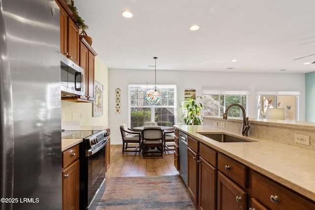 kitchen with light countertops, hanging light fixtures, appliances with stainless steel finishes, a sink, and hardwood / wood-style floors