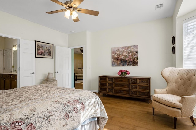 bedroom featuring ensuite bathroom, wood finished floors, visible vents, and a ceiling fan