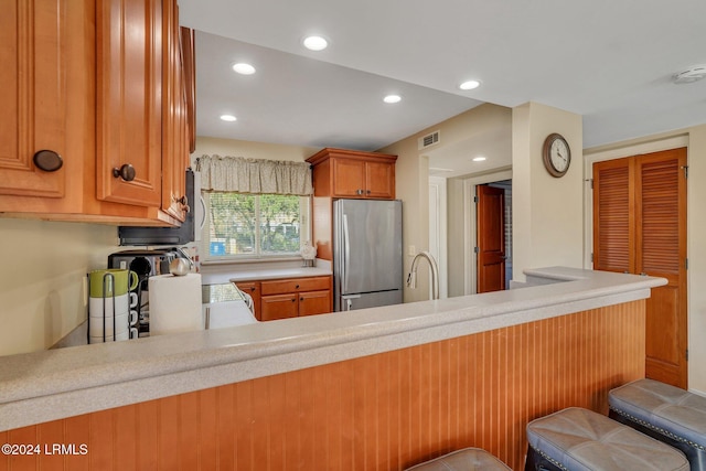 kitchen with stainless steel refrigerator, a breakfast bar, kitchen peninsula, and sink