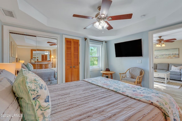 bedroom with multiple closets, ceiling fan, wood-type flooring, and a raised ceiling