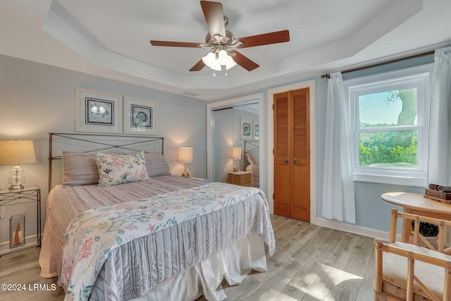 bedroom with light hardwood / wood-style floors, ceiling fan, and a tray ceiling