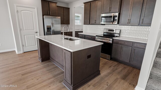 kitchen with stainless steel appliances, dark brown cabinets, sink, and a center island with sink