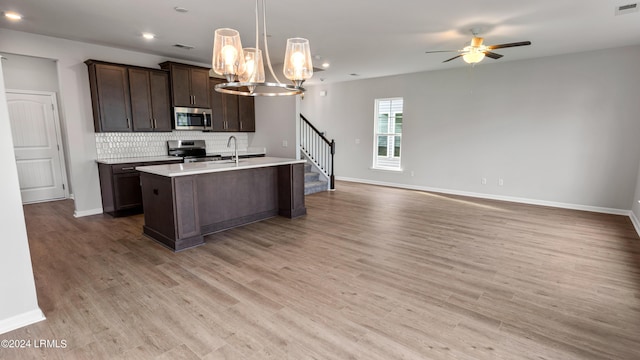 kitchen featuring dark brown cabinetry, decorative light fixtures, light wood-type flooring, stainless steel appliances, and decorative backsplash