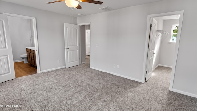 unfurnished bedroom featuring ensuite bath, ceiling fan, light carpet, a spacious closet, and a closet