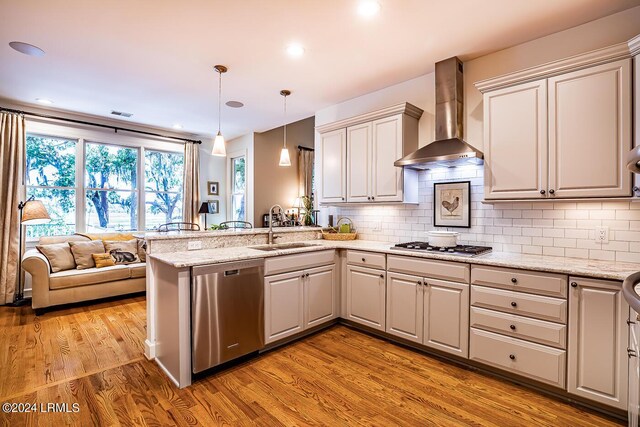 kitchen featuring pendant lighting, sink, kitchen peninsula, stainless steel appliances, and wall chimney exhaust hood