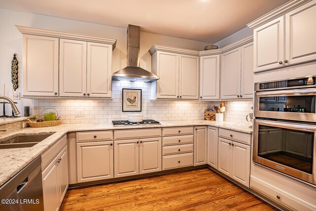 kitchen with sink, appliances with stainless steel finishes, backsplash, light hardwood / wood-style floors, and wall chimney exhaust hood