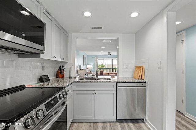 kitchen with light stone counters, decorative backsplash, stainless steel appliances, and light hardwood / wood-style floors