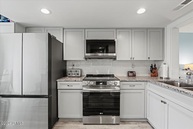 kitchen with light stone counters, sink, tasteful backsplash, and appliances with stainless steel finishes