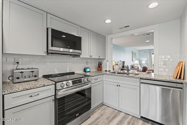 kitchen featuring light stone counters, sink, light hardwood / wood-style floors, and appliances with stainless steel finishes