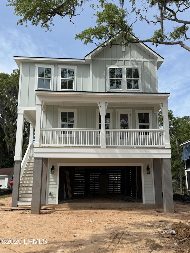 coastal home featuring driveway, board and batten siding, a porch, a garage, and stairs