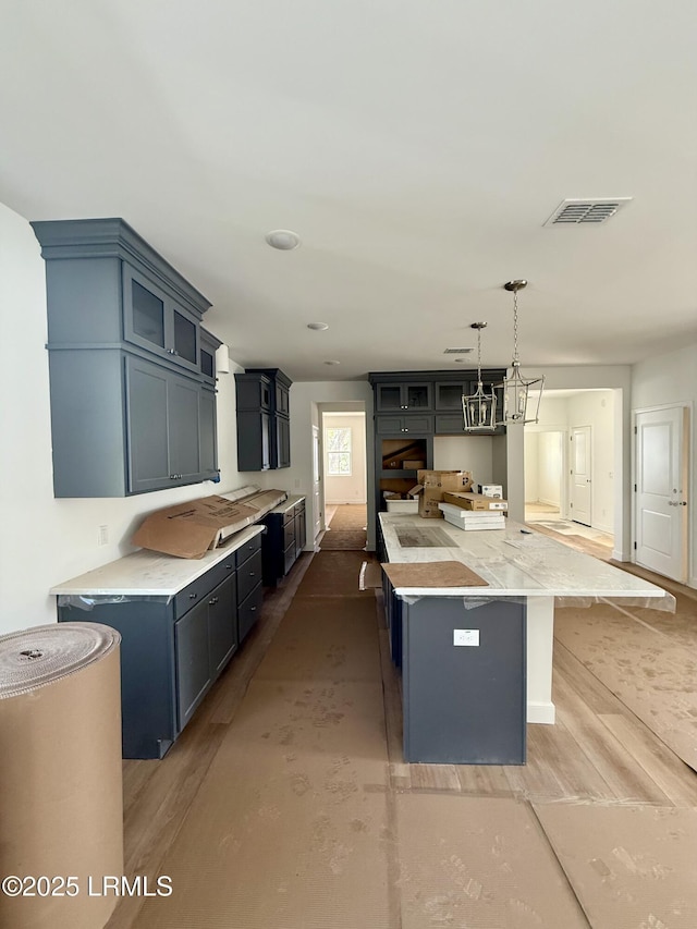kitchen featuring light wood-style flooring, a spacious island, visible vents, and glass insert cabinets